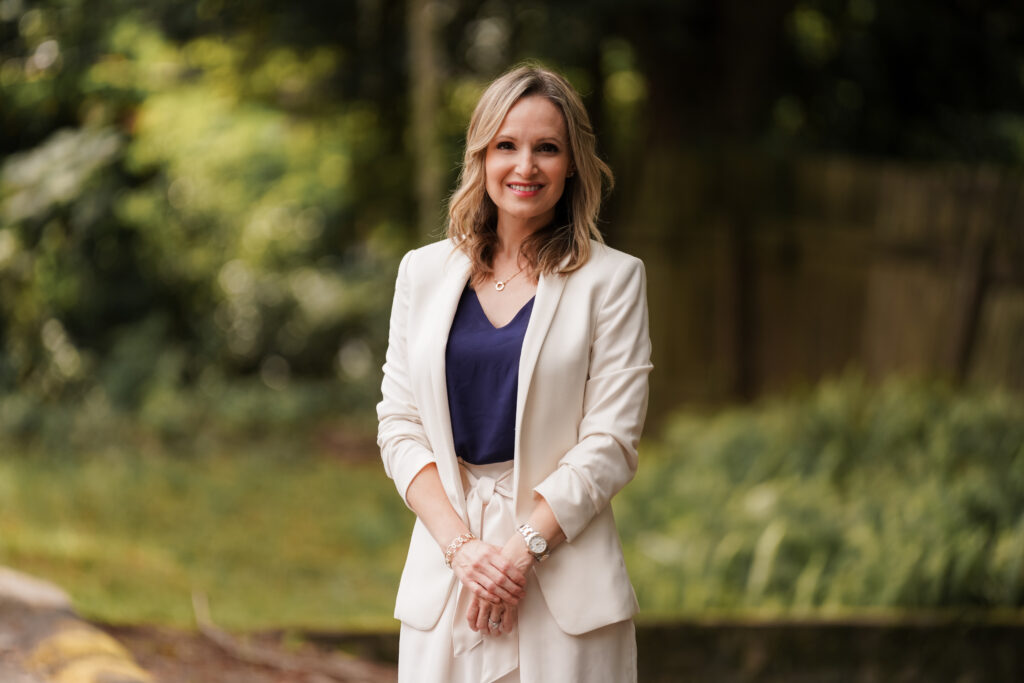 Managing Partner, Christin Gonzalez, standing outside, smiling, with greenery behind her