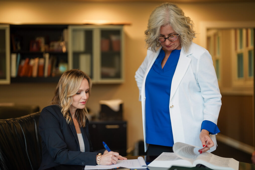 Female attorneys Shannon Novey and Cristin Gonzalez, in their office, reviewing legal documentation, Gonzalez is sitting, Novey is standing